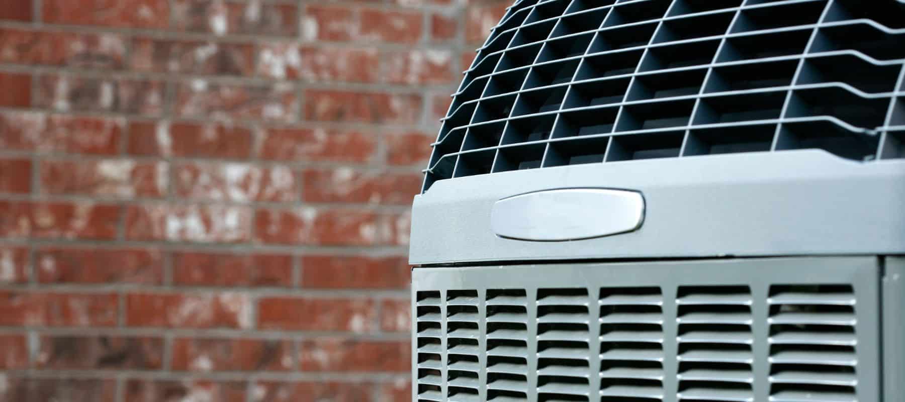 a gray outdoor hvac system against the side of a red brick home