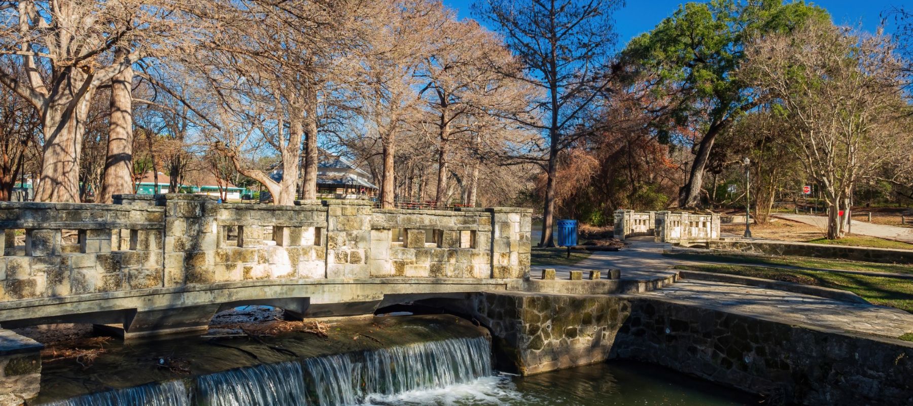 a park bridge going over a stream with trees behind it