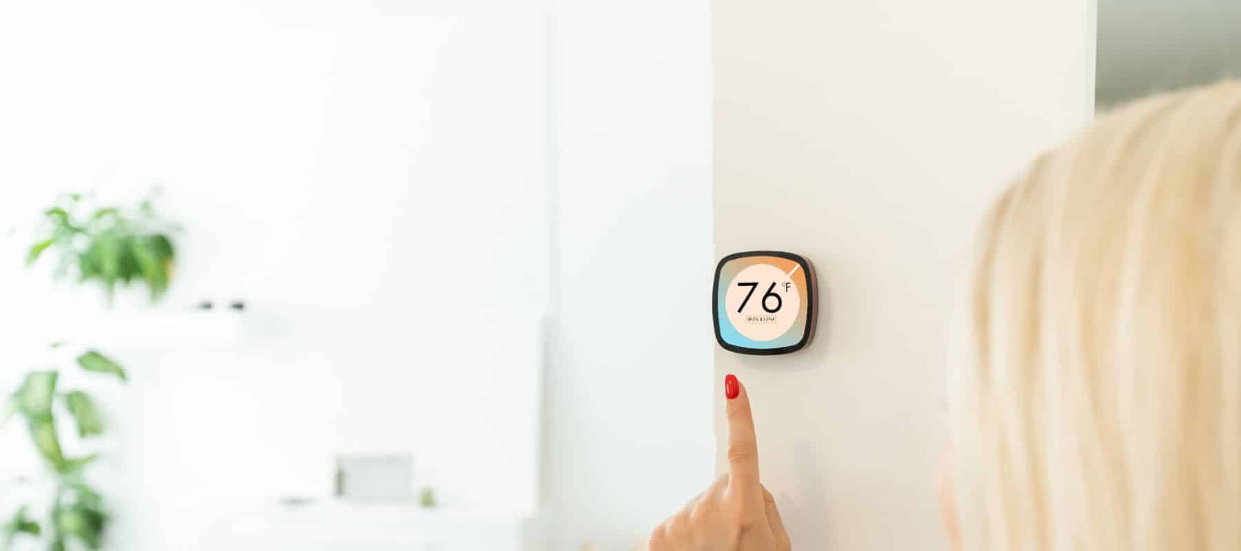 closeup of a smart thermostat that's about to be adjusted by a woman with red finger nails