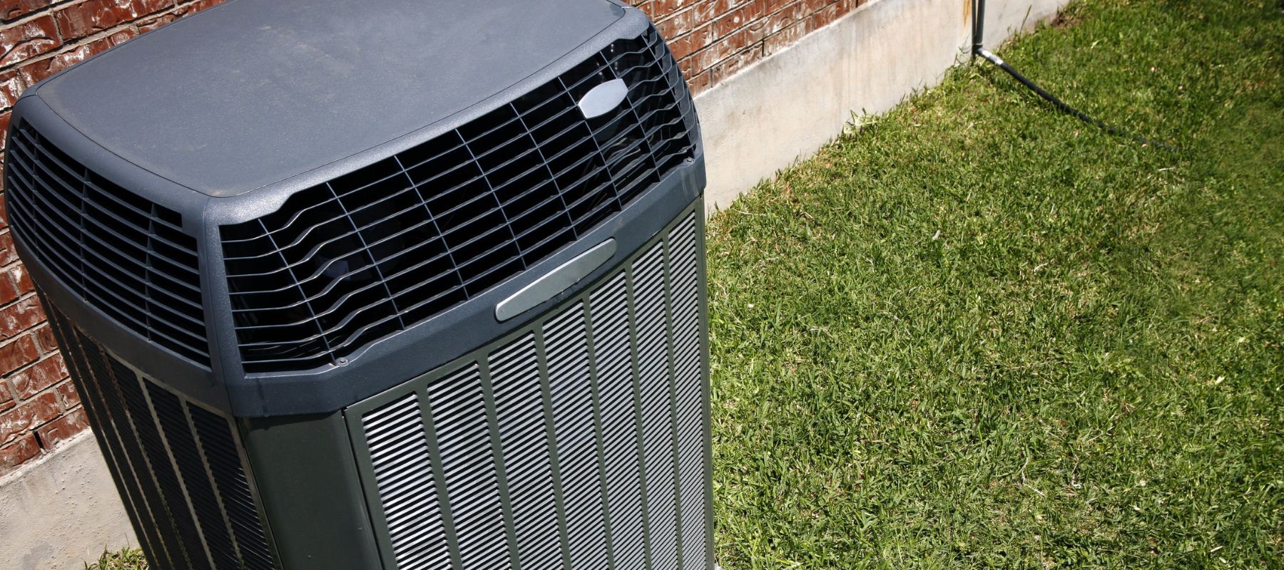 an outdoor air conditioner surrounded by green grass and a red brick home