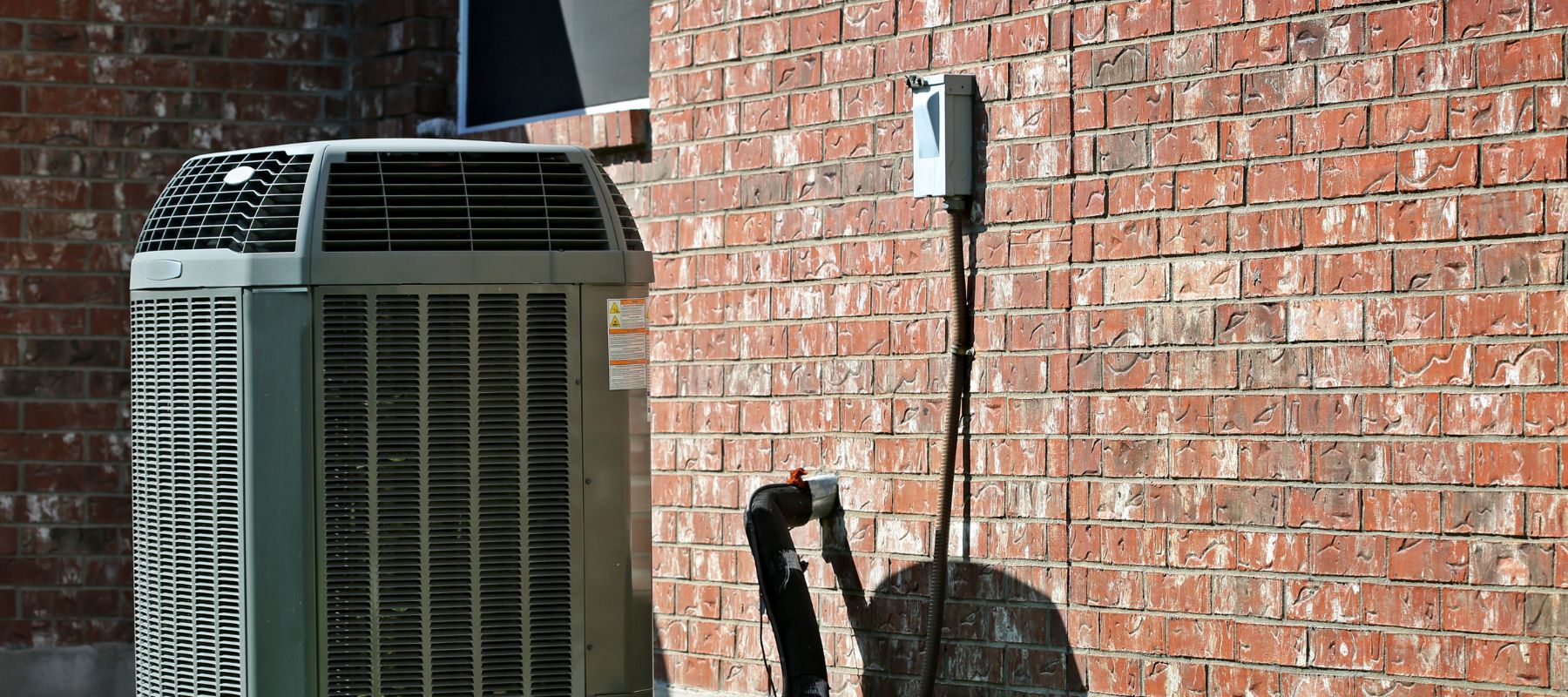 a gray outdoor ac system installed to a red brick wall of a San Antonio home