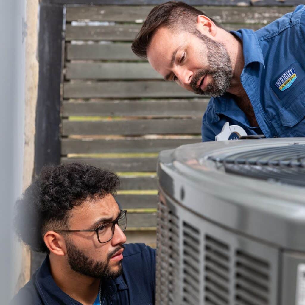 wright ac technicians collaborating on a residential outdoor hvac unit repair