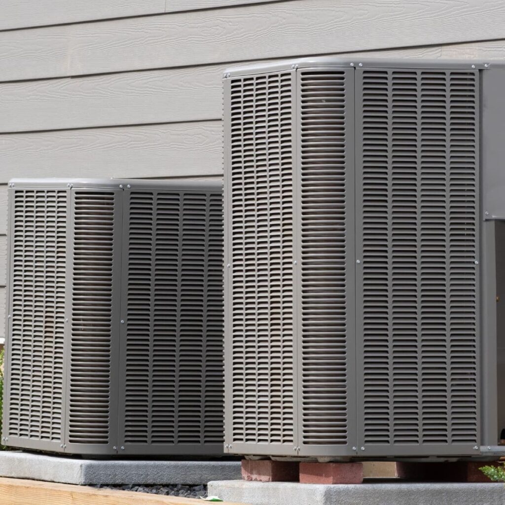 outdoor heat pump systems on the side of a gray San Antonio home