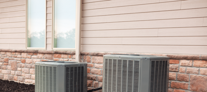 two outdoor hvac units against a peach colored wall