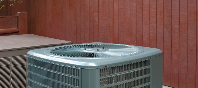 a gray outdoor ac unit next to a red wall