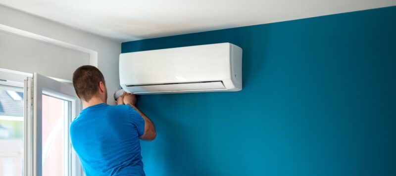 man in a blue shirt installing a ductless AC unit onto a blue wall