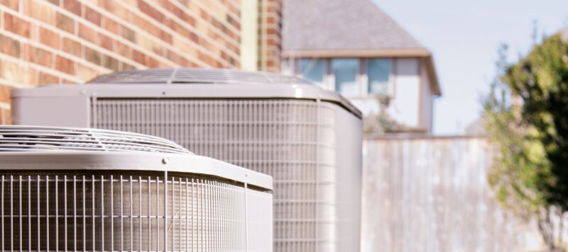 two outdoor hvac systems side by side against the brick wall of a home