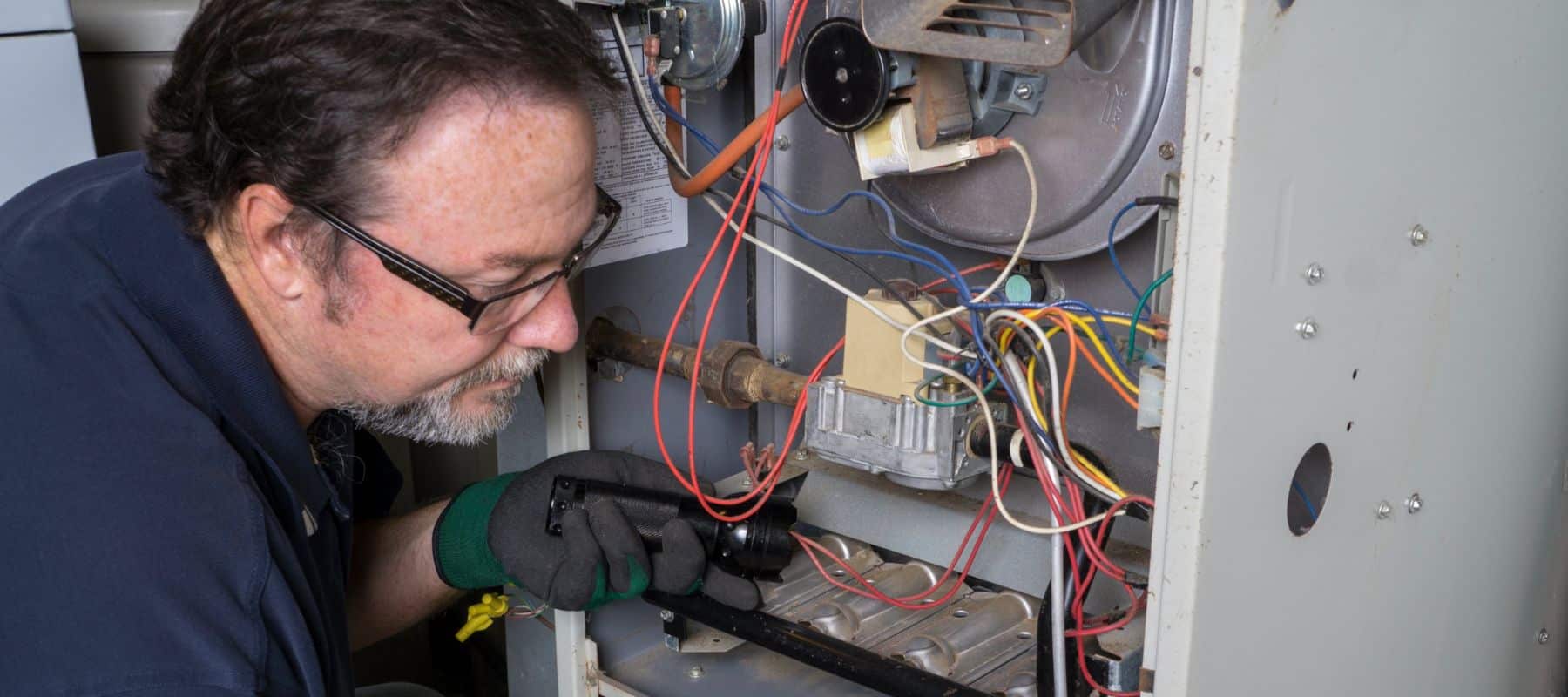 hvac technician leaning down to inspect the inside of a furnace