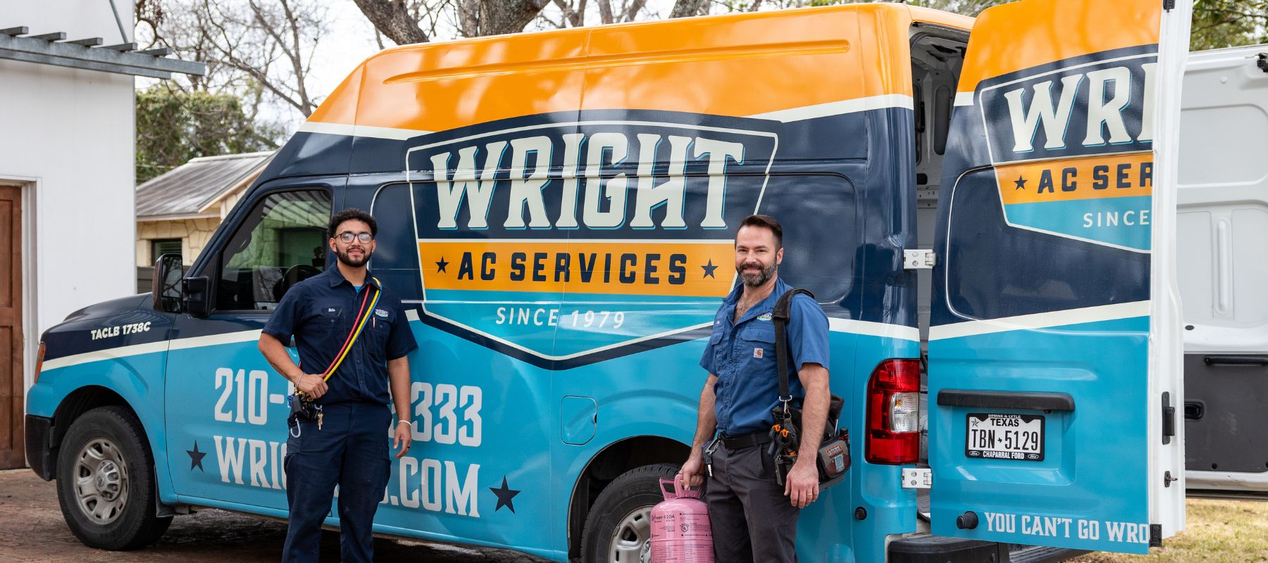 two wright ac services technicians posing in front of the company van with different equipment for the job hanging off of their shoulders like a tool bag and wires