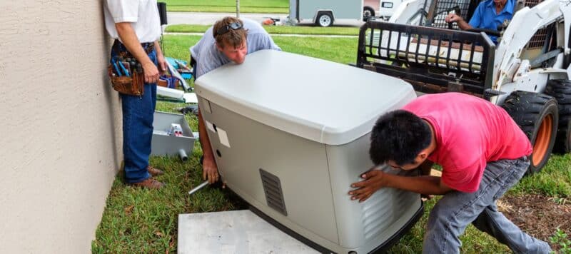 techs lifting a backup power generator for installation on a home
