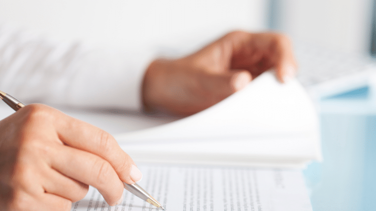 hands holding paperwork on a desk and a pen pointing to the paper