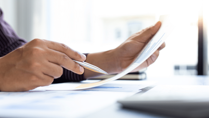Hands holding up paperwork and pointing a pen to the paper
