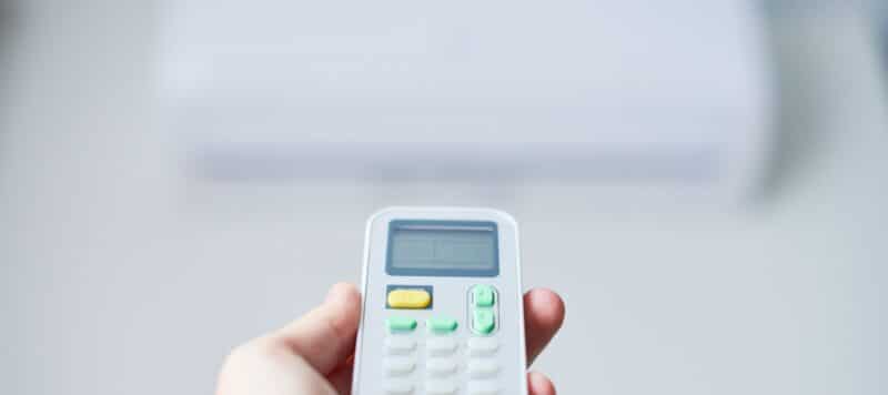 Close-up of a hand holding a digital remote control with buttons and a display screen, against a blurred background, highlighting the device in focus used for adjusting settings remotely