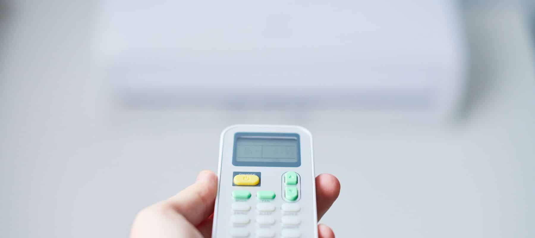 Close-up of a hand holding a digital remote control with buttons and a display screen, against a blurred background, highlighting the device in focus used for adjusting settings remotely
