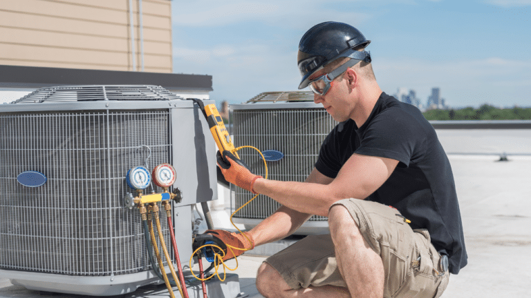 A male HVAC technician inspecting a large outdoor unit on top of a building.