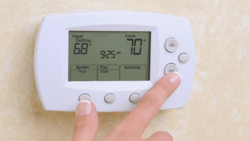 A traditional thermostat on a wall with a hand pressing the buttons.