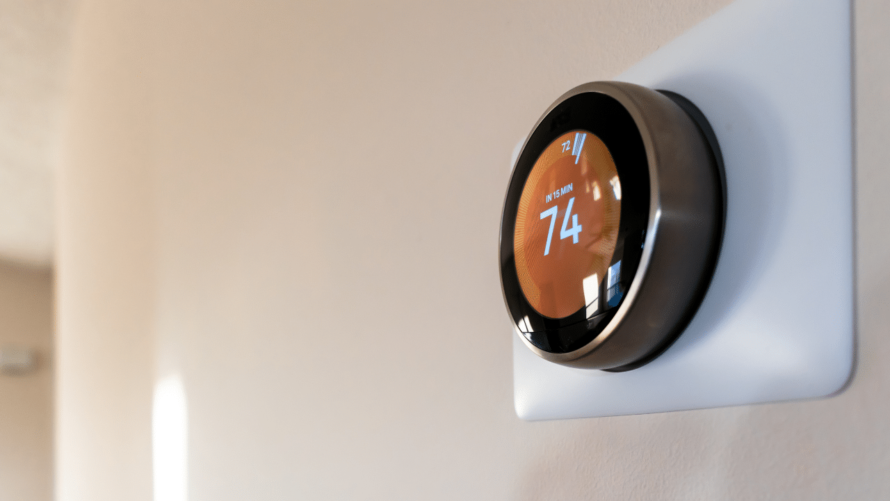 A smart thermostat mounted on a wall with the temperature of 74 showing.