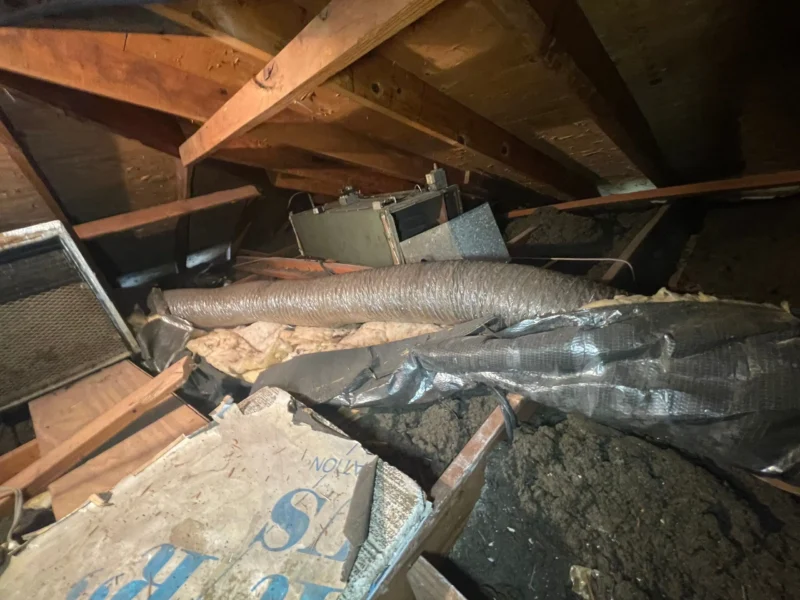 Cluttered attic with insulation and debris.