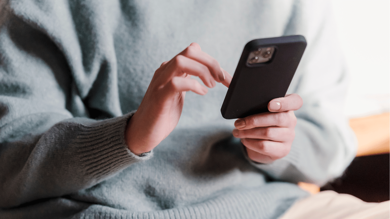 A person in a grey sweater holding a black smart phone scrolling.