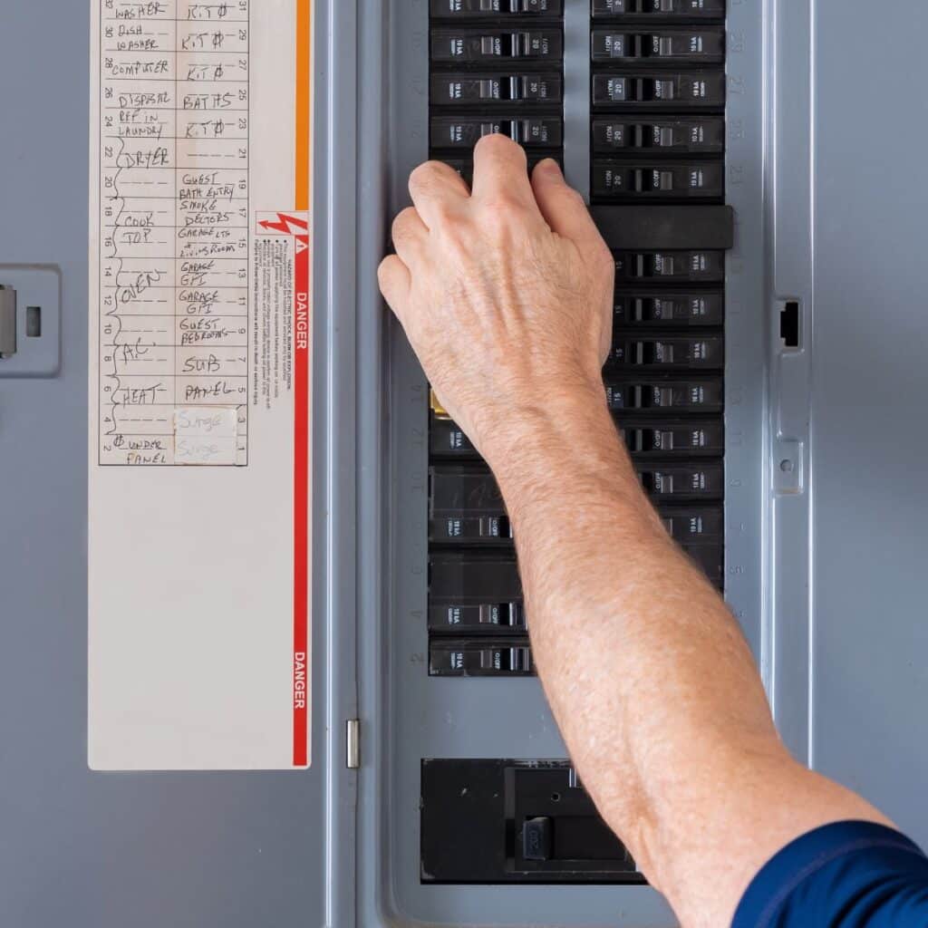 Close-up of a hand flipping a switch on a labeled electrical panel