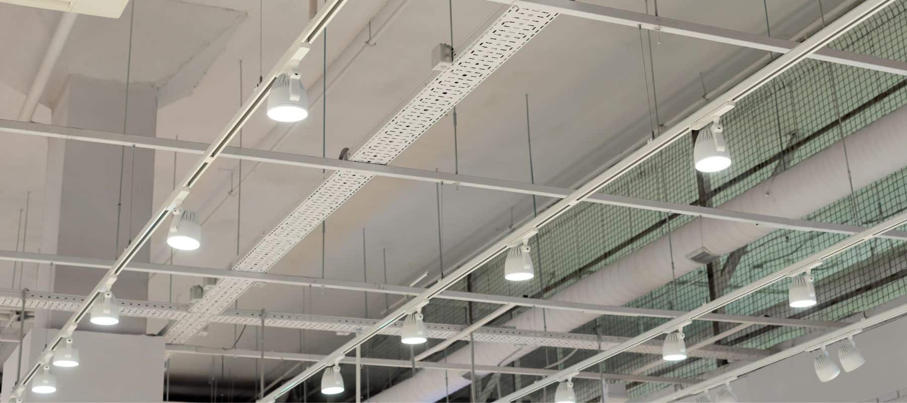 Ceiling view of commercial track lighting and exposed ductwork in an industrial space