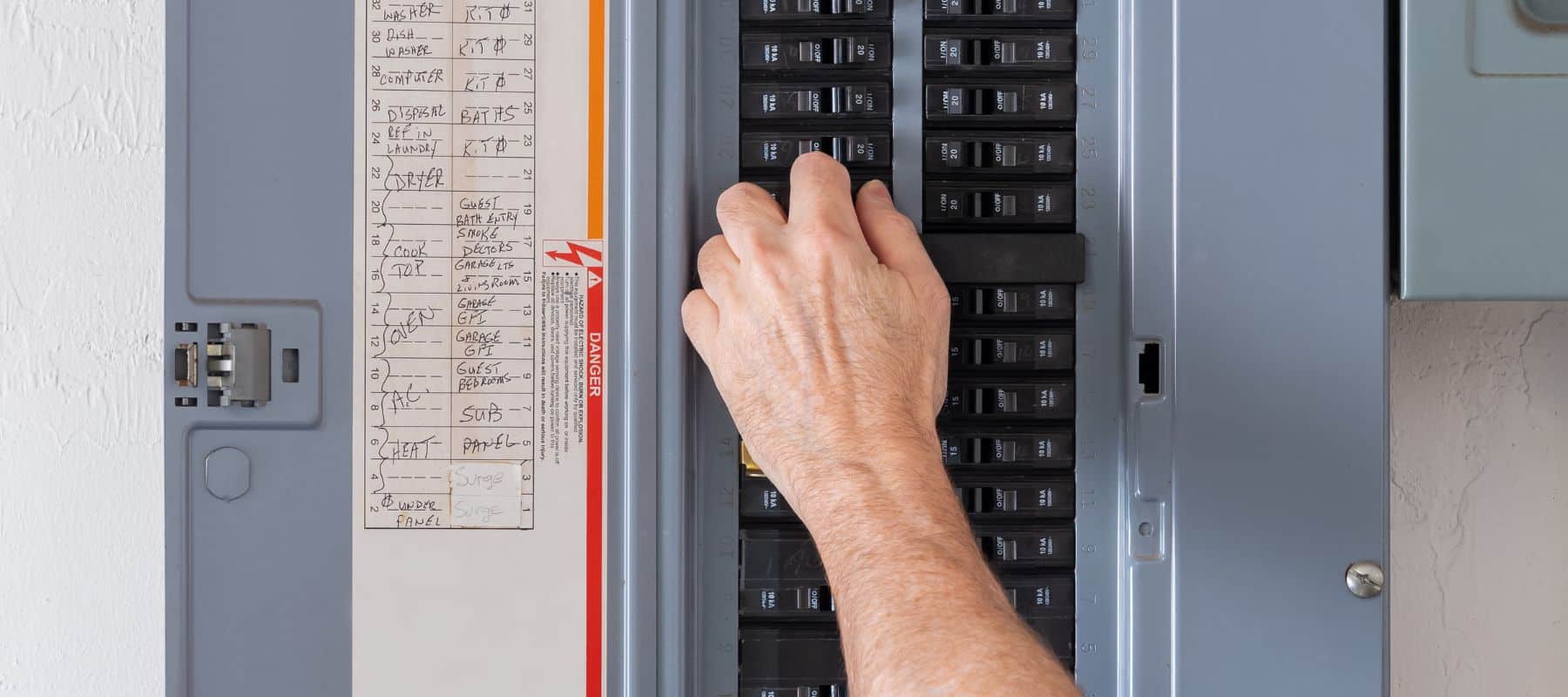 Close-up of a hand flipping a switch on a labeled electrical panel