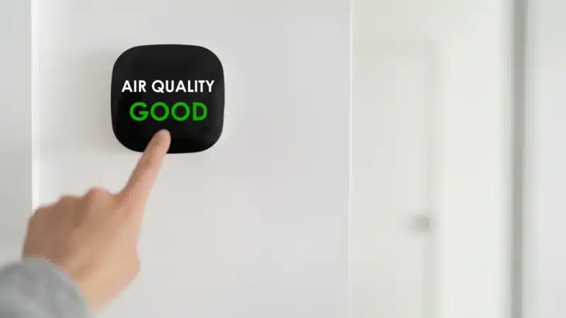 A hand pointing at a thermostat on a wall that reads "Air quality good"