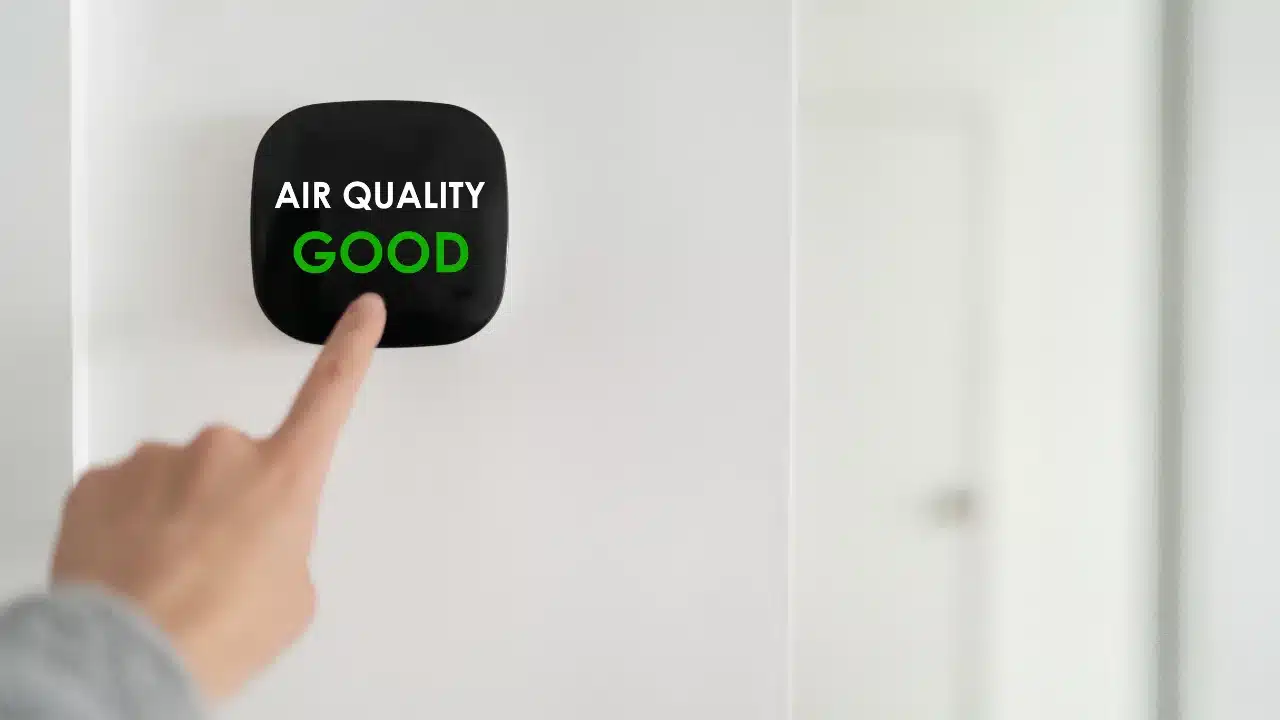 A hand pointing at a thermostat on a wall that reads "Air quality good"