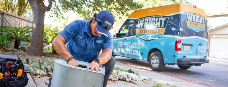 A Wright technician working on an AC part with a truck in the background.